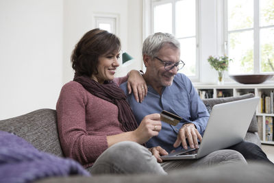 Smiling mature couple at home on the sofa shopping online