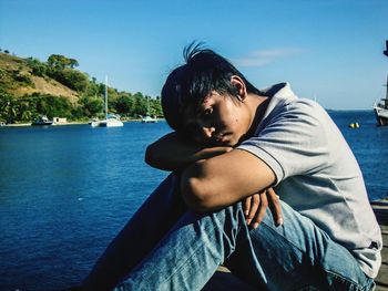 Portrait of young man sitting on pier over sea against sky