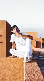 Portrait of smiling young man with hand on chin sitting on concrete wall