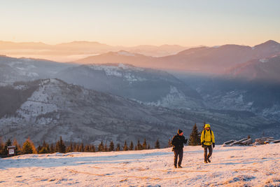 Rear view of men walking on snowcapped mountain against sky during sunset