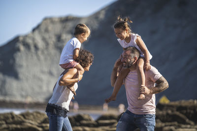 Cheerful parents carrying children on shoulder at beach