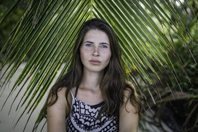 Portrait of beautiful young woman against palm leaves