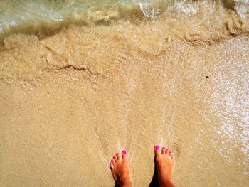 Low section of young woman standing on shore at beach
