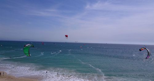 Parachutes flying over sea against sky at beach