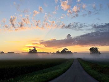 Road amidst field against sky during sunset