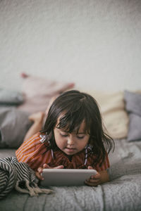 Down syndrome girl using digital tablet while lying on sofa at home