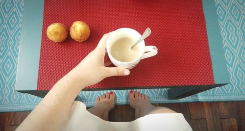 Low section of woman holding milk in cup by cupcakes on table