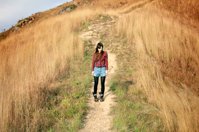 Young woman standing on field amidst dry grass