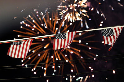 Low angle view of american flags hanging against firework display at night