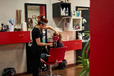 Hairdresser with a face shield dries her client's hair in her salon