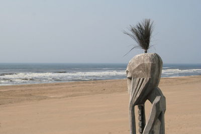 Rear view of statue on beach against clear sky