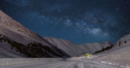 Road amidst snowcapped mountains against sky at night