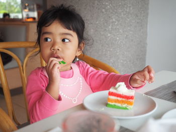 A beautiful asian kid girl with black hair wearing pink color shirt eating a rainbow cake