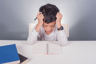 Tensed boy studying at table against wall