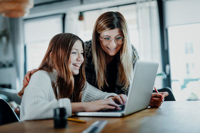 Young woman using phone while sitting on laptop