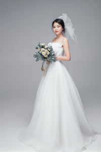 Portrait of bride with bouquet standing against gray background