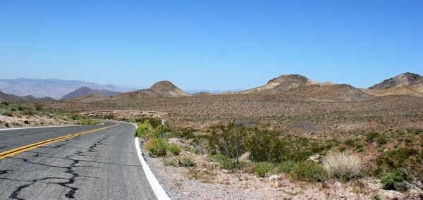 Empty road by mountains against clear blue sky