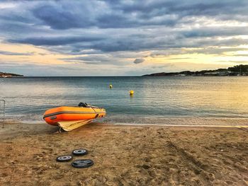 Boat moored on beach against sky during sunset