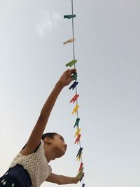 Low angle view of girl holding colorful clothespins on clothesline against sky