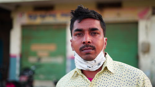 Front shot of indian man wearing mask and shirt over blur market background with serious face.