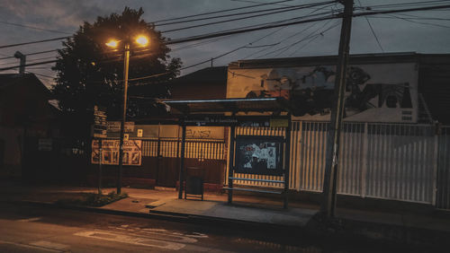 Illuminated street light by building against sky at night