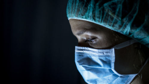 Portrait of young female surgeon, wearing mask and a surgical mask, in front of black background
