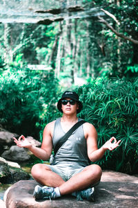 Young man sitting on sunglasses against plants