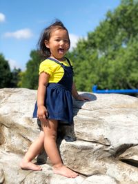 Cute smiling girl standing on rock against sky
