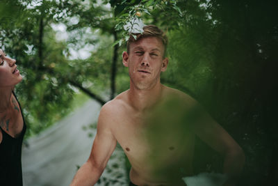 Young man looking away while standing against trees