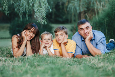 Beautiful happy caucasian family of four people lying on a ground in park on summer day. 