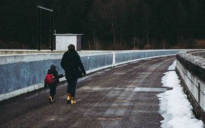 Rear view of mother and daughter walking on road during winter