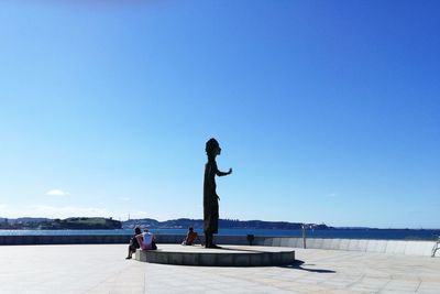 People standing on shore against clear blue sky