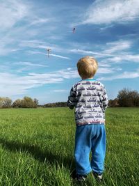 Rear view of boy standing on field against sky