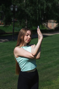 Young caucasian long-haired woman in sportswear is doing yoga in public park. outdoor workout. 