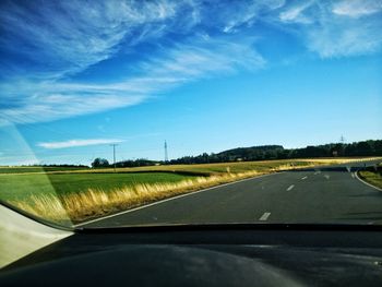 Road amidst field seen through car windshield