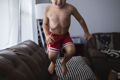 Shirtless boy jumping on couch at home