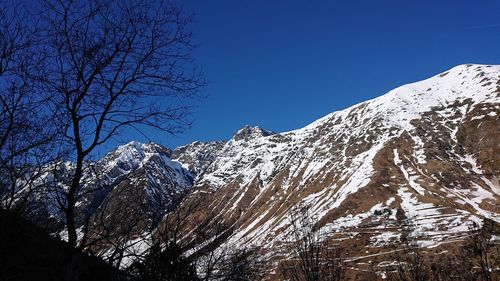 Low angle view of snowcapped mountains against clear blue sky