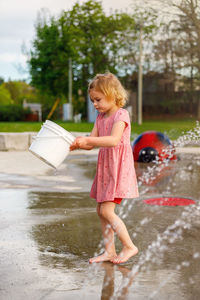 Child playing with bucket at splash pad playground in water park. girl near fountains in summertime