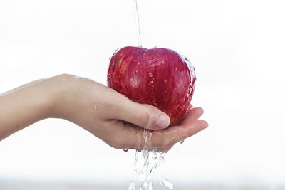 Close-up of hand holding strawberry over white background
