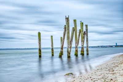 Wooden posts on beach against sky