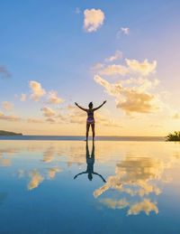 Rear view of woman standing in sea against sky during sunset