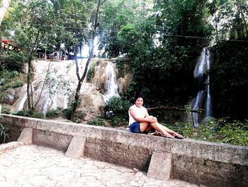 Young woman sitting on rock against trees