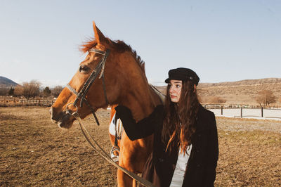 Young woman looking away while standing with horse in animal pen