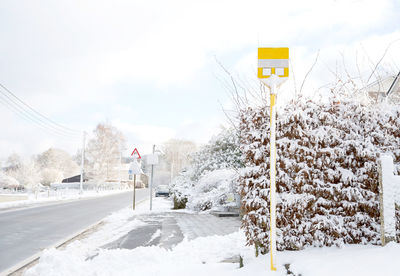 Road sign by snow covered trees against sky