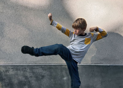 Boy kicking by gray wall