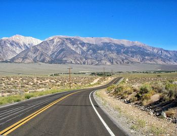 Empty road by mountains against clear blue sky