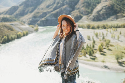 Carefree brunette young woman traveler in poncho from back on background of mountain river