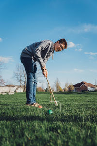 Teen boy playing croquet outside on the grass on a sunny day.