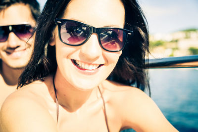 Portrait of smiling young woman wearing sunglasses against sky
