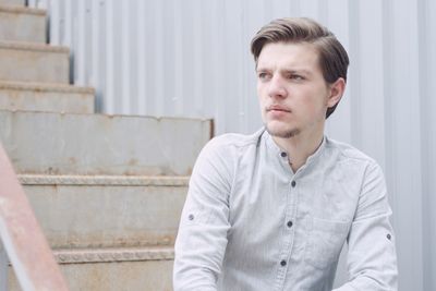 Thoughtful young man looking away while sitting on steps